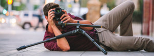 Fotografo di matrimonio appoggiato a terra con la sua macchina fotografica su un treppiede che fa un contrapposto