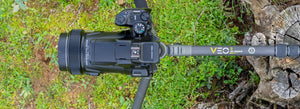 Treppiede Veo 3GO con fotocamera con le gambe spiegate su un prato e un tronco