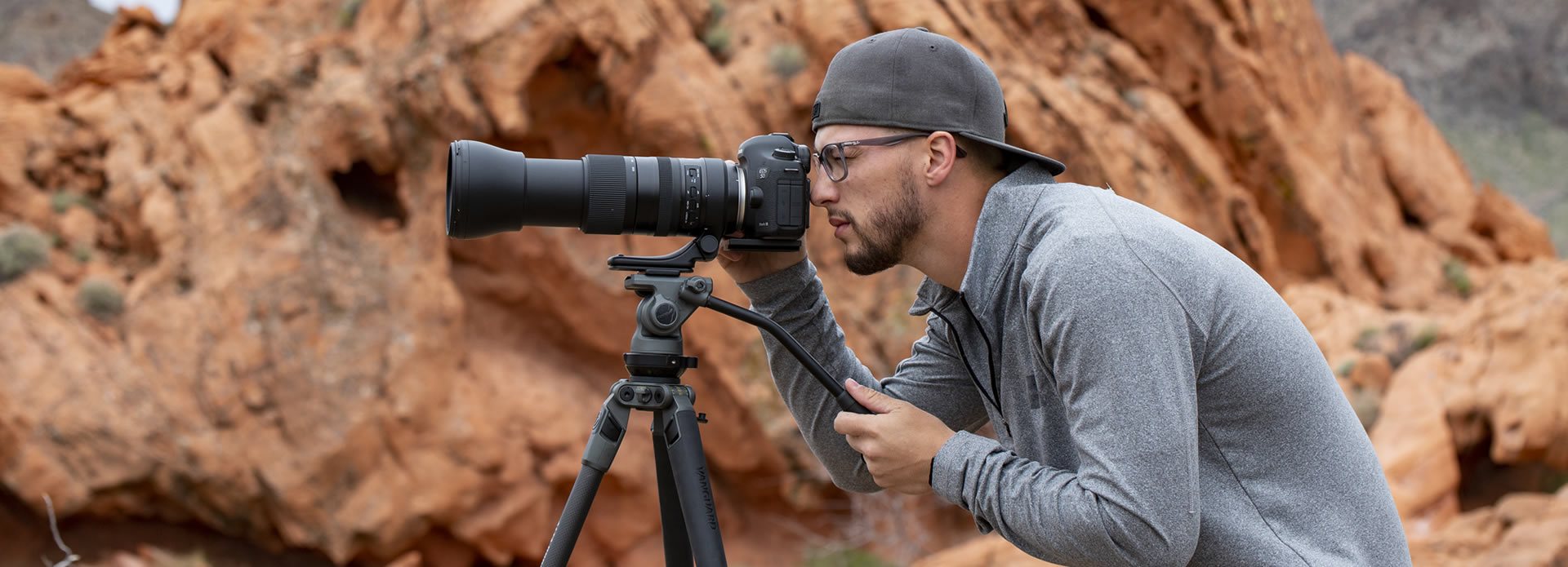 Fotografo sportivo che scatta con la sua fotocamera e l'obiettivo su un treppiede video.
