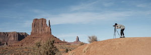 Fotografo naturalista che usa la sua macchina fotografica su un treppiede per scattare una foto in una zona desertica.