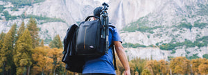 Fotografo con lo zaino della macchina fotografica sulla schiena che cammina su una montagna