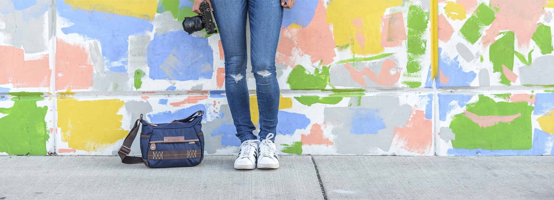 Fotografo appoggiato ad un muro con la sua macchina fotografica accanto alla sua borsa Messenger